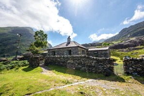 A stone house with a thatched roof, surrounded by a stone wall and a grassy path. - 2 Bed in Nant Peris (oc-wag693) (Nant Peris)