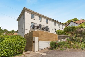 A two-story residential building with a balcony, a garage, and a garden with various plants and flowers. - 2 Bed in Beer (oc-jbchur) (Beer)