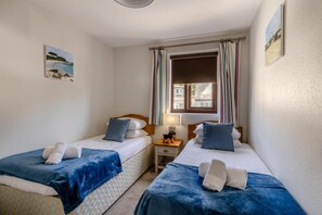 A room with two beds, each with a blue blanket and pillows, a nightstand with a lamp, and a window with curtains. - 2 Bed in Beer (oc-jbpion) (Beer)