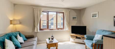 A living room with a sofa, a coffee table, a television, and a window with curtains.