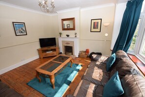 Una sala de estar con sofá, mesa de centro, televisión, chimenea y una ventana con cortinas.