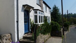 A two-story house with a blue door and white walls, located on a quiet street with a stone wall and a clear sky. - 3 Bed in Beer (oc-jbpurl) (Beer)