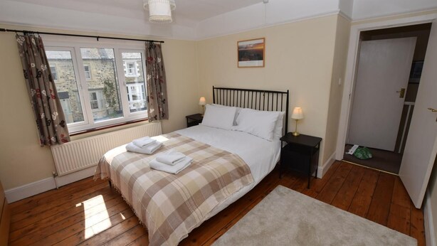 A bedroom with a bed, two bedside tables, a window with curtains, a radiator, a door, and a small rug. - 3 Bed in Beer (oc-jbpurl) (Beer)