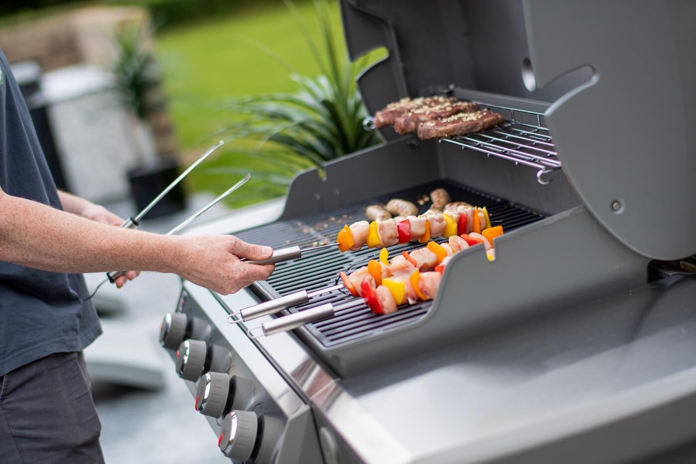 A person grilling meat and vegetables on an outdoor grill.