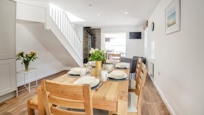 A modern dining area with a wooden table set for four, white walls, and a staircase leading to another level. - 3 Bed in Talwrn (oc-bow229) (Ysgubor Hen)