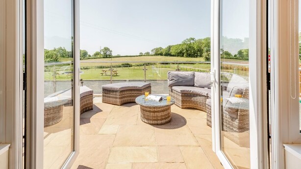 A balcony with wicker furniture, a glass table, and a view of a grassy field. - 3 Bed in Talwrn (oc-bow229) (Ysgubor Hen)