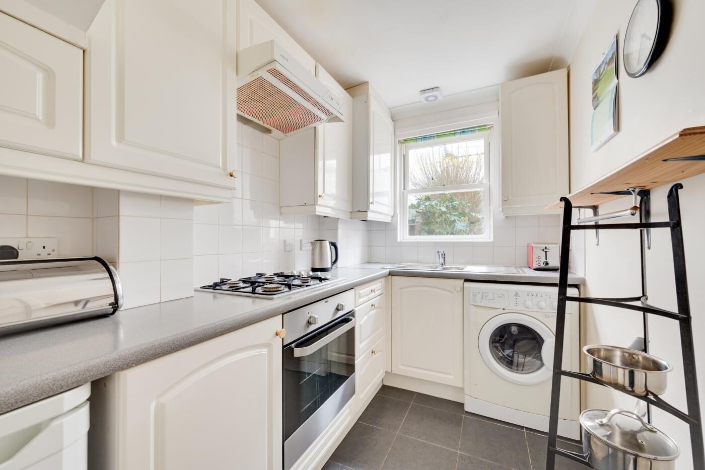 A compact kitchen with white cabinetry, a gas stove, a built-in oven, a washing machine, and a metal drying rack.