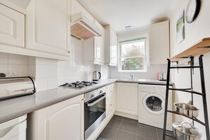A compact kitchen with white cabinetry, a gas stove, a built-in oven, a washing machine, and a metal drying rack. - 2 Bed in Brighton (oc-bbivy2) (Hove)