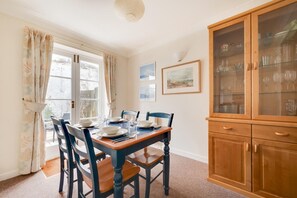 A dining area with a wooden table set for four, flanked by chairs, a cabinet with glass doors, and a window with curtains. - 2 Bed in Brighton (oc-bbivy2) (Hove)