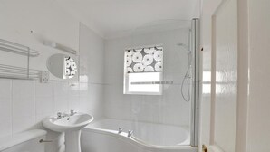 Et badeværelse med toilet, håndvask, badekar og brusebad.