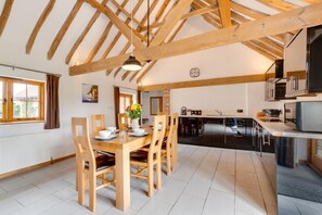 A spacious kitchen with modern appliances, a dining area with wooden furniture, and a view of the adjacent living room. - 3 Bed in Rye (oc-rh1137) (Brede)