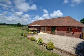 A brick house with a tiled roof, a gravel driveway, and a small garden area with shrubs and a patio table. - 3 Bed in Rye (oc-rh1137) (Brede)