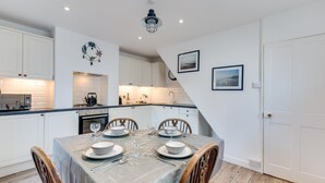 A modern kitchen with white cabinets, a dining table set for four, and a small island with a kettle. - 2 Bed in Deal (oc-cc0163) (Kingsdown)