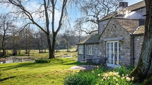 Ein Steinhaus mit einem Steinkamin, eine Wiese mit Narzissen und ein Teich im Hintergrund.