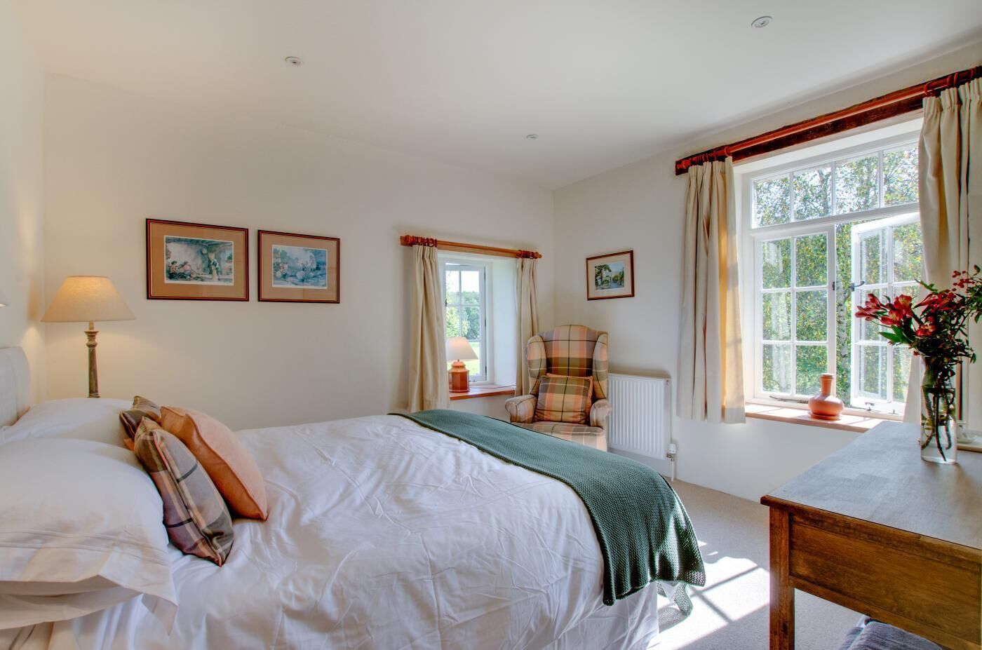 A bedroom with a bed, a chair, a table, and a window with curtains.