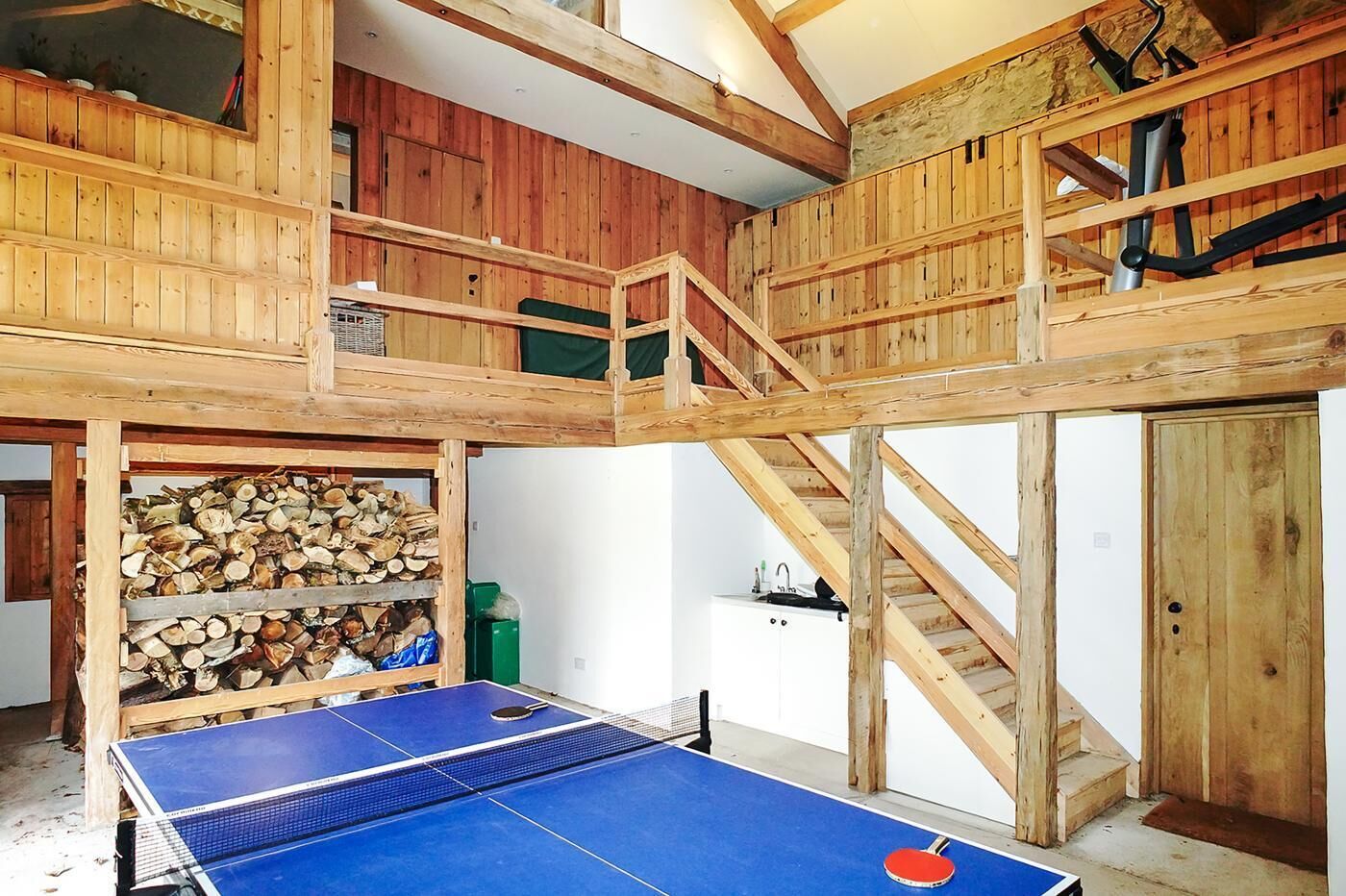 A multi-level wooden structure with a ping pong table, a staircase, and a stack of firewood.