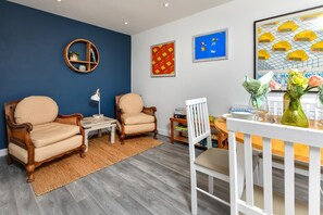 A modern living room with two beige armchairs, a small table, a white dining table with chairs, and a bookshelf. - 1 Bed in Pwllheli (oc-7marin) (Pwllheli)