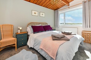 Une chambre à coucher avec un lit, une chaise, une table de chevet et une fenêtre donnant sur un beau paysage.