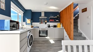 A compact kitchen with a washing machine, oven, and a wooden staircase leading to a landing. - 1 Bed in Pwllheli (oc-7marin) (Pwllheli)