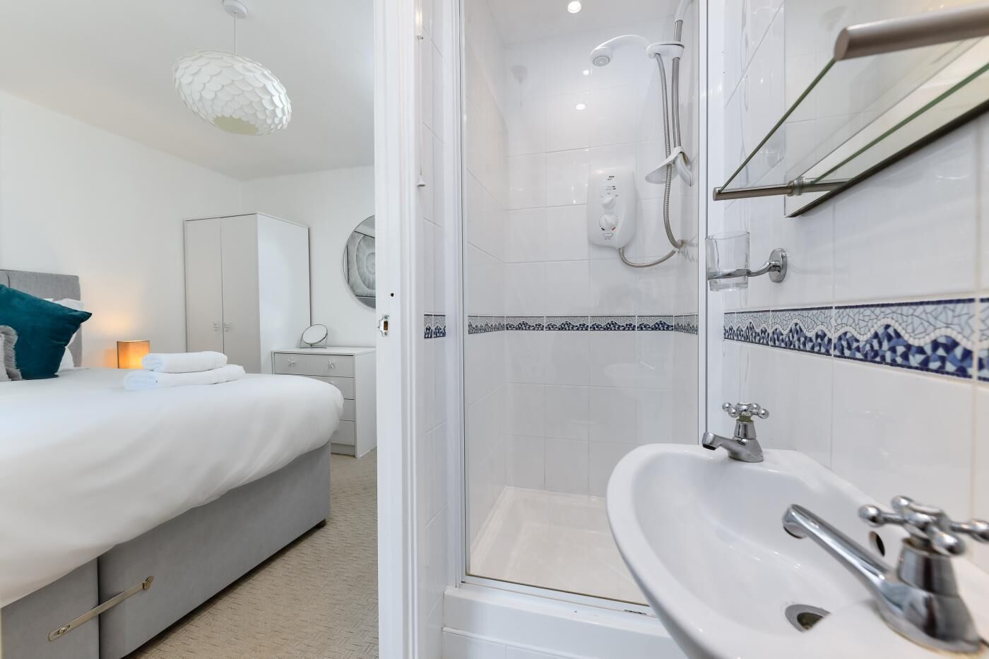 A modern hotel room with a bed, bedside table, and a shower area with a glass door.