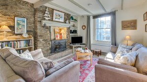 A cozy living room with a stone wall, fireplace, bookshelves, and comfortable seating. - 2 Bed in Fowey (oc-secret) (Fowey)