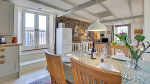 A modern kitchen with a stone wall, a dining area with a table set for four, and a cozy living area with a sofa and a TV. - 2 Bed in Fowey (oc-secret) (Fowey)