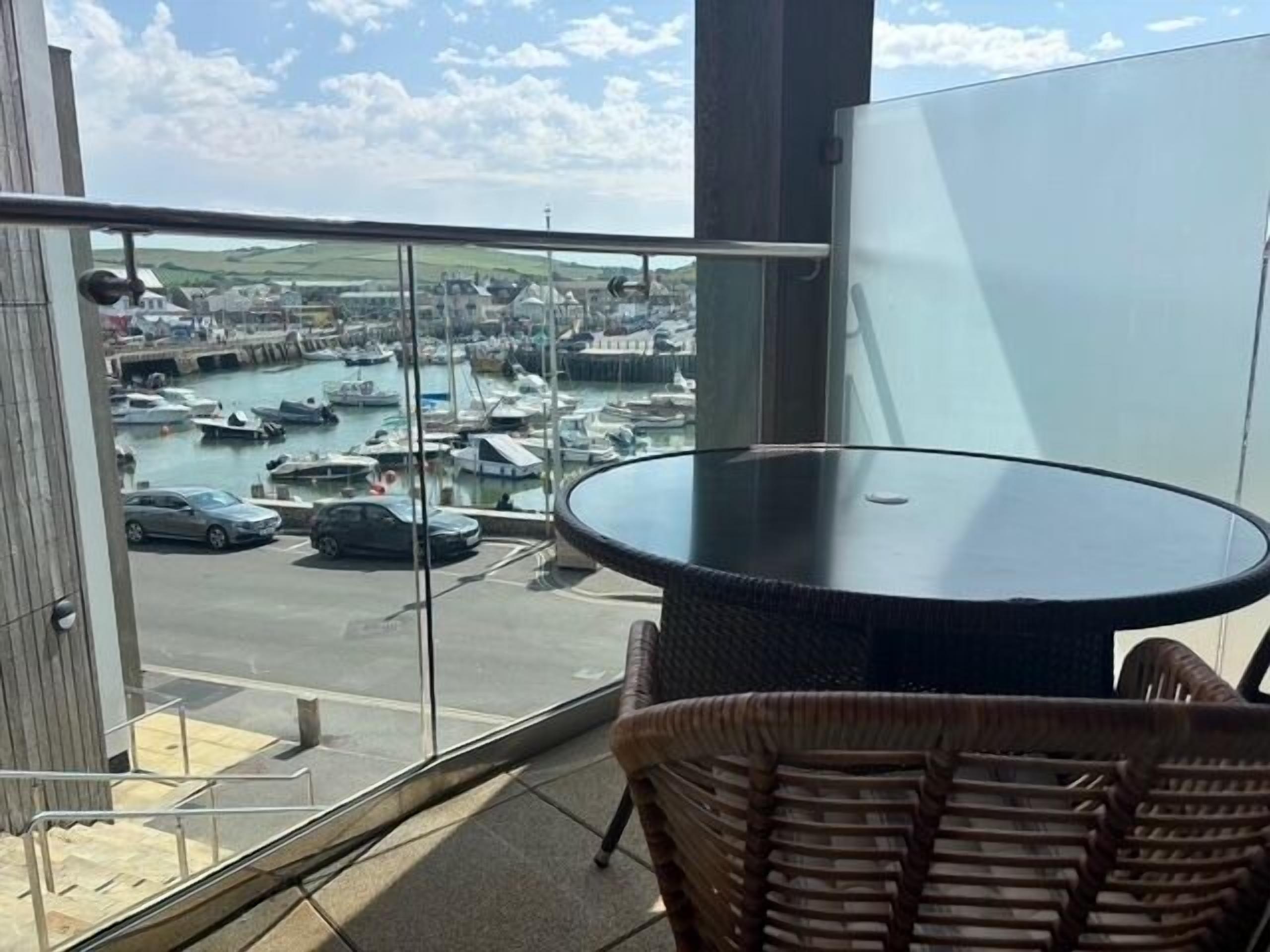A balcony with a glass railing overlooking a marina with boats and cars.