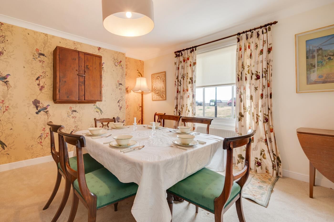 Une salle à manger avec une table ronde dressée pour quatre personnes, entourée de chaises en bois recouvertes d’un tissu vert.