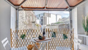 Un balcon agrémenté d’une séparation en treillis de bois, de deux fauteuils confortables, d’une petite table avec une bouteille et un verre, et de plantes en pot.