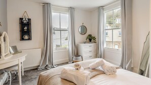 Une chambre à coucher avec un lit, une commode, un miroir, un bureau et une fenêtre avec des rideaux.