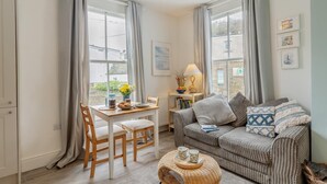 Un salon chaleureux avec un canapé à rayures, une table à manger avec des chaises et une table basse en osier.