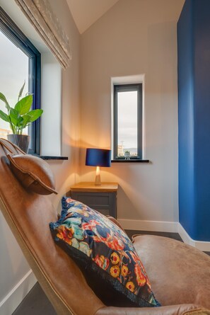 A room with a reclining chair, a small table with a lamp, a window with a view, and a potted plant. - 1 Bed in Caernarfon (oc-bow270) (Penygroes)