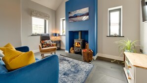 A modern living room with a fireplace, a blue accent wall, a sofa with yellow cushions, and a wooden coffee table. - 1 Bed in Caernarfon (oc-bow270) (Penygroes)