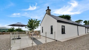 A modern house with a white exterior, a gravel driveway, a wooden table and chairs, and a large umbrella. - 1 Bed in Caernarfon (oc-bow270) (Penygroes)