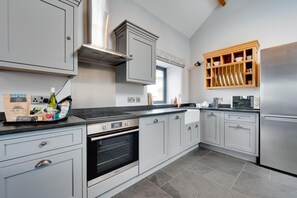 A modern kitchen with grey cabinetry, a built-in oven, a stainless steel refrigerator, and a wooden shelf above the sink. - 1 Bed in Caernarfon (oc-bow270) (Penygroes)