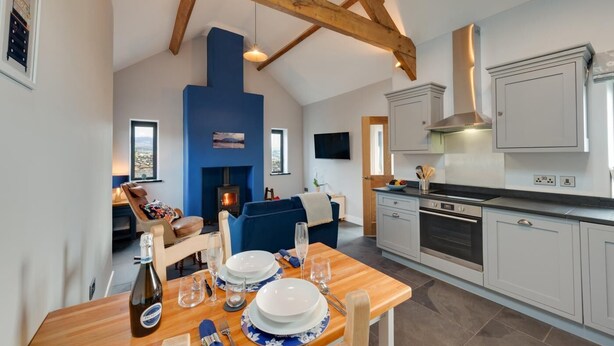 A modern kitchen with white cabinets, a built-in stove, and a dining area with a wooden table set for four. - 1 Bed in Caernarfon (oc-bow270) (Penygroes)