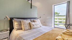 A bedroom with a bed, a bedside lamp, a window with a view, and a wooden floor. - 1 Bed in Aberaeron (oc-bow300) (Llwyncelyn)