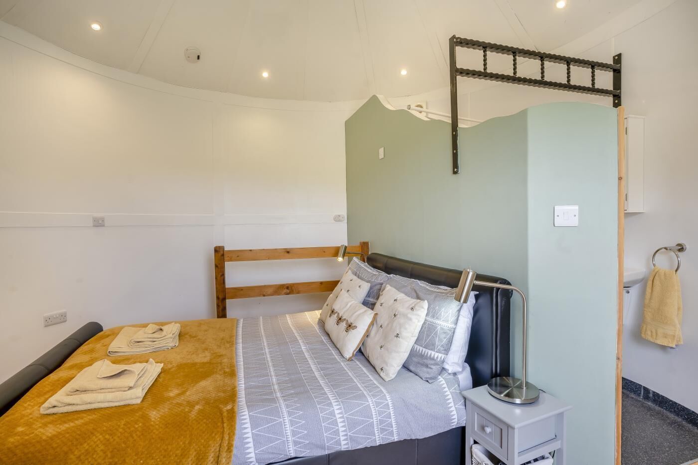 A bedroom with a bed, a nightstand, a lamp, a towel rack, and a headboard with a pull-up bar.