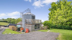 A rustic cabin with a cylindrical silo, a wooden deck, and a gravel driveway. - 1 Bed in Aberaeron (oc-bow300) (Llwyncelyn)