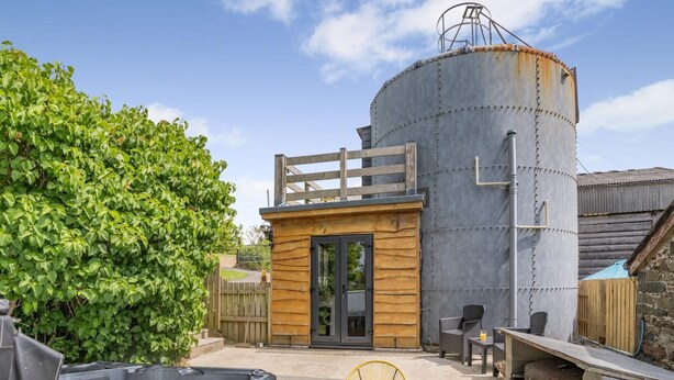 A compact outdoor area with a hot tub, seating, and a large cylindrical structure, likely a water tank. - 1 Bed in Aberaeron (oc-bow300) (Llwyncelyn)