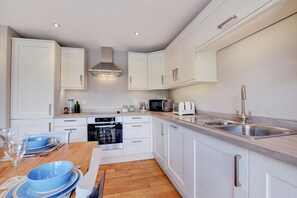 A modern kitchen with white cabinetry, a built-in oven, a microwave, a toaster, and a stainless steel sink. - 3 Bed in Kingswear (oc-bc1104) (Dartmouth)