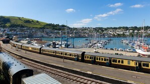 Ein Bahnhof mit Blick auf einen Hafen, Boote und eine Stadt im Hintergrund.