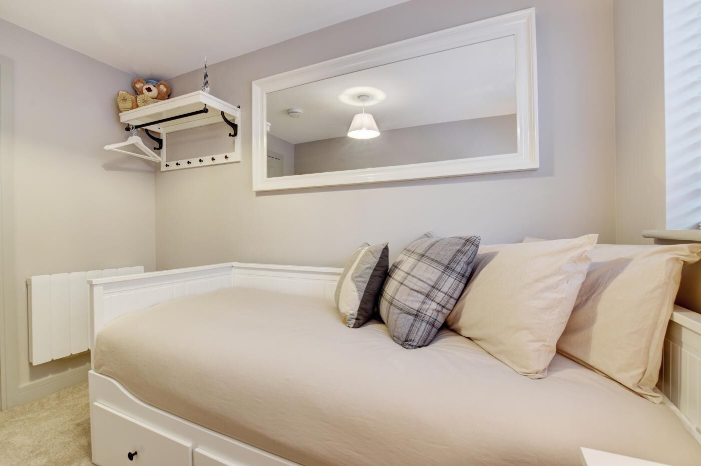 A bedroom with a bed, a hanging shelf with toys, a mirror, and a ceiling light.