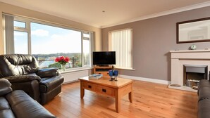 Ein Wohnzimmer mit einer Ledersofa, einem Holztisch, einem Flachbildfernseher, einem Kamin und großen Fenstern mit Aussicht.