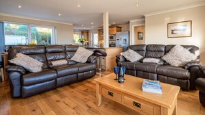 Ein modernes Wohnzimmer mit zwei Ledersofas, einem Holztisch und einer Küche im Hintergrund.