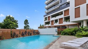 A modern building with a swimming pool, outdoor seating, and greenery. - The Corso - Central Maroochydore Apartment (Sunshine Coast)