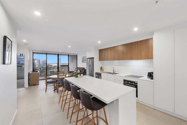 A modern kitchen with a central island, white cabinetry, and a large window providing a view of the city.