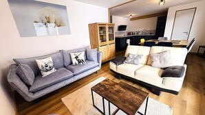 A living room with two sofas, a coffee table, and a kitchen in the background. - Le refuge d'Anny - Three Bedroom Apartment, Sleeps 8 (Vaujany)