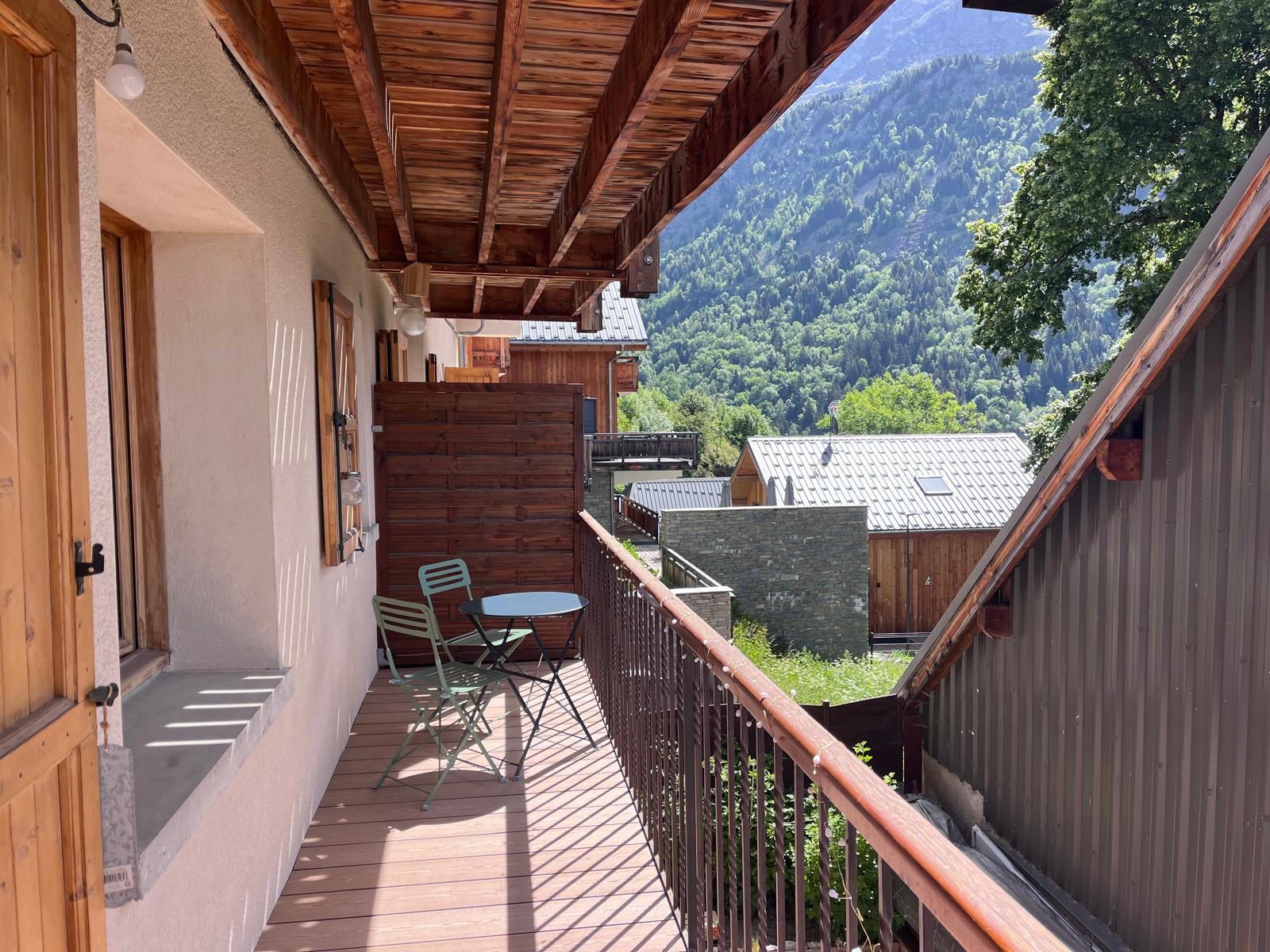 A wooden balcony with a view of a mountainous landscape, a small table with chairs, and a wooden fence.