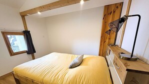 A single bed with a wooden headboard, a bedside table with a lamp, and a window with curtains. - Le refuge d'Anny - Three Bedroom Apartment, Sleeps 8 (Vaujany)